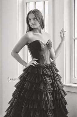 black and white image of a young lady in a dark gown in soft window light.